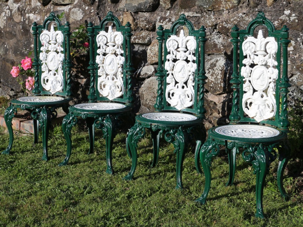 A set of four Victorian cast iron garden chairs featuring white openwork backrests with central medallion cameos framed by dark green structural frames and cabriole legs. View VI