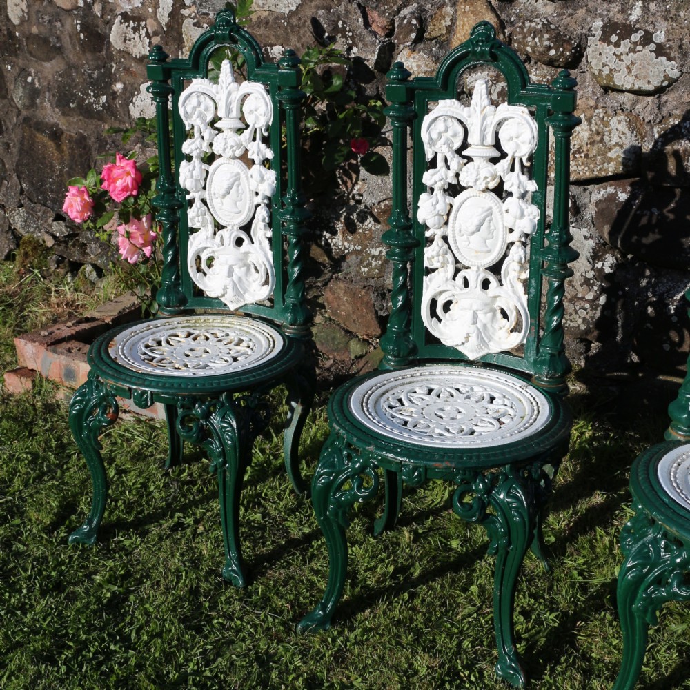 A set of four Victorian cast iron garden chairs featuring white openwork backrests with central medallion cameos framed by dark green structural frames and cabriole legs. View VIII