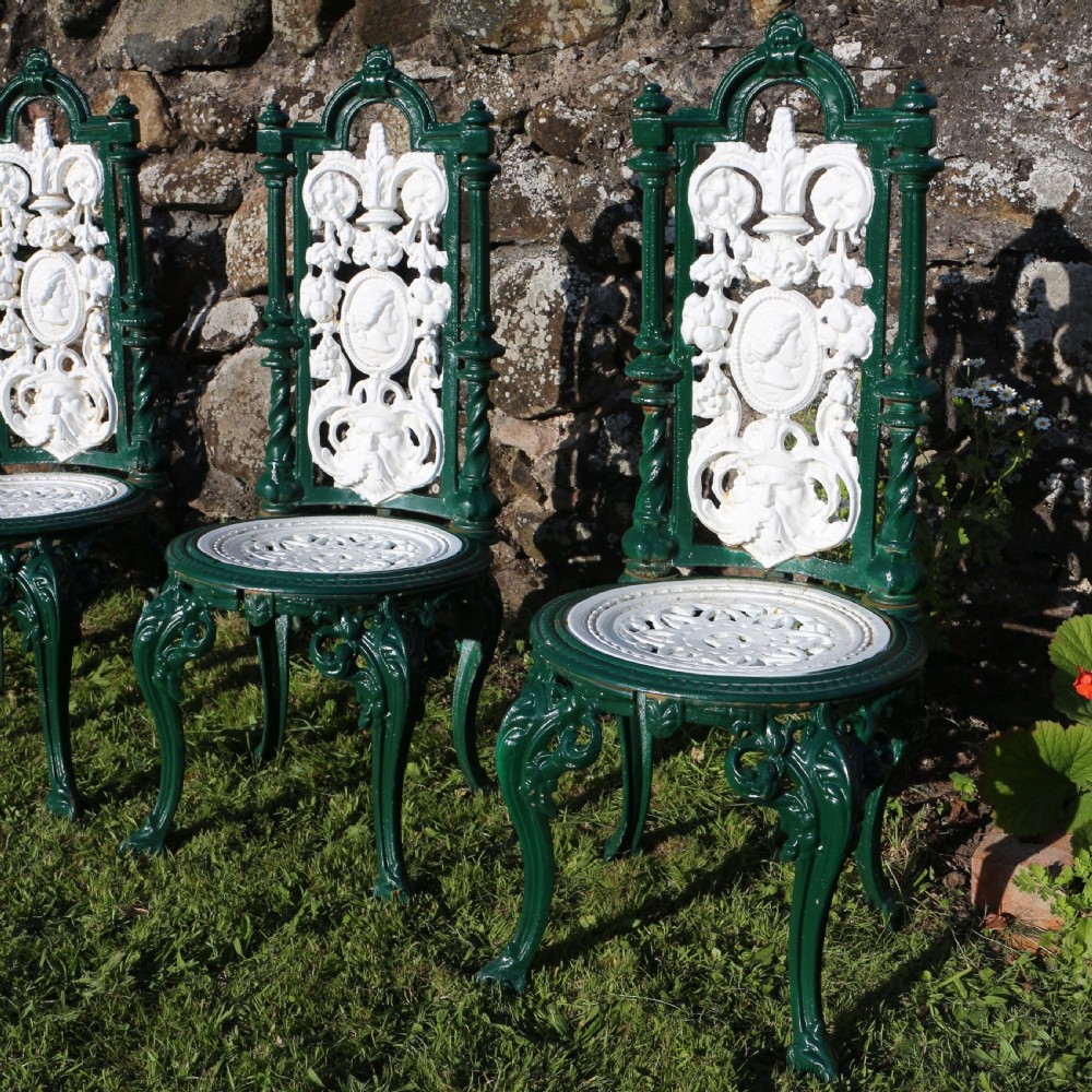 A set of four Victorian cast iron garden chairs featuring white openwork backrests with central medallion cameos framed by dark green structural frames and cabriole legs. View IX