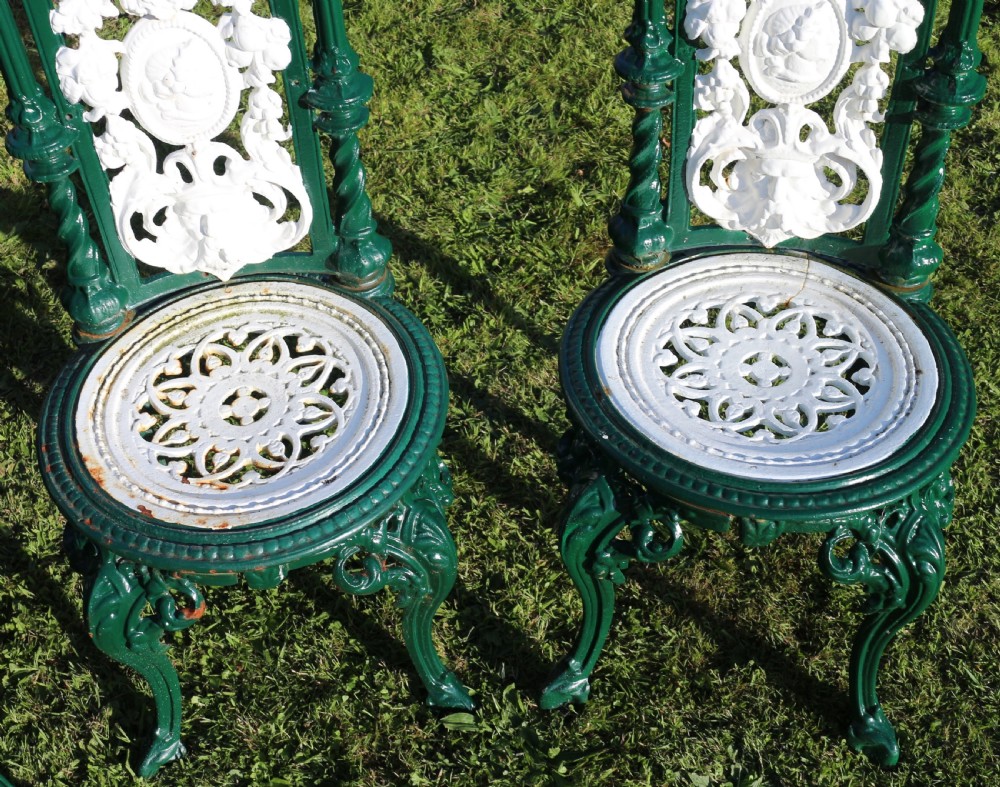 A set of four Victorian cast iron garden chairs featuring white openwork backrests with central medallion cameos framed by dark green structural frames and cabriole legs. View XI