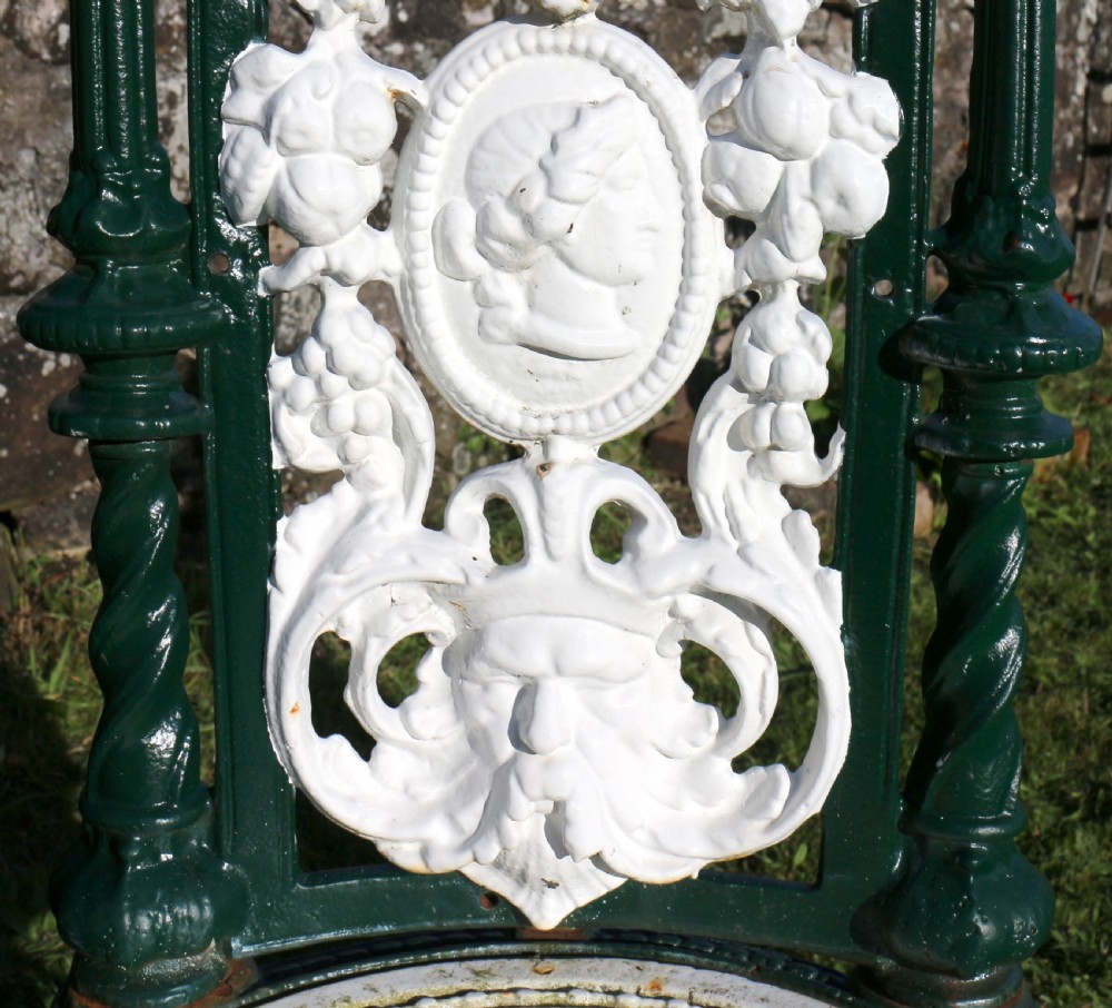 A set of four Victorian cast iron garden chairs featuring white openwork backrests with central medallion cameos framed by dark green structural frames and cabriole legs. View XIV