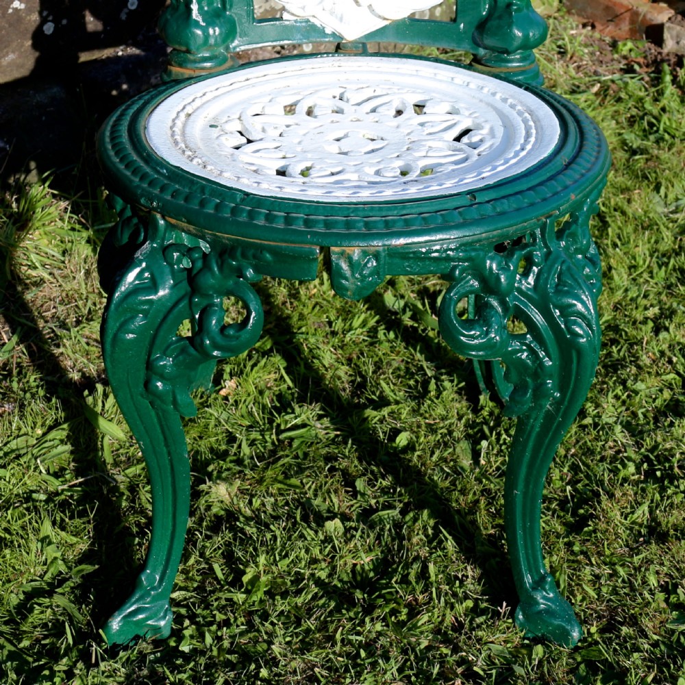 A set of four Victorian cast iron garden chairs featuring white openwork backrests with central medallion cameos framed by dark green structural frames and cabriole legs. View XV