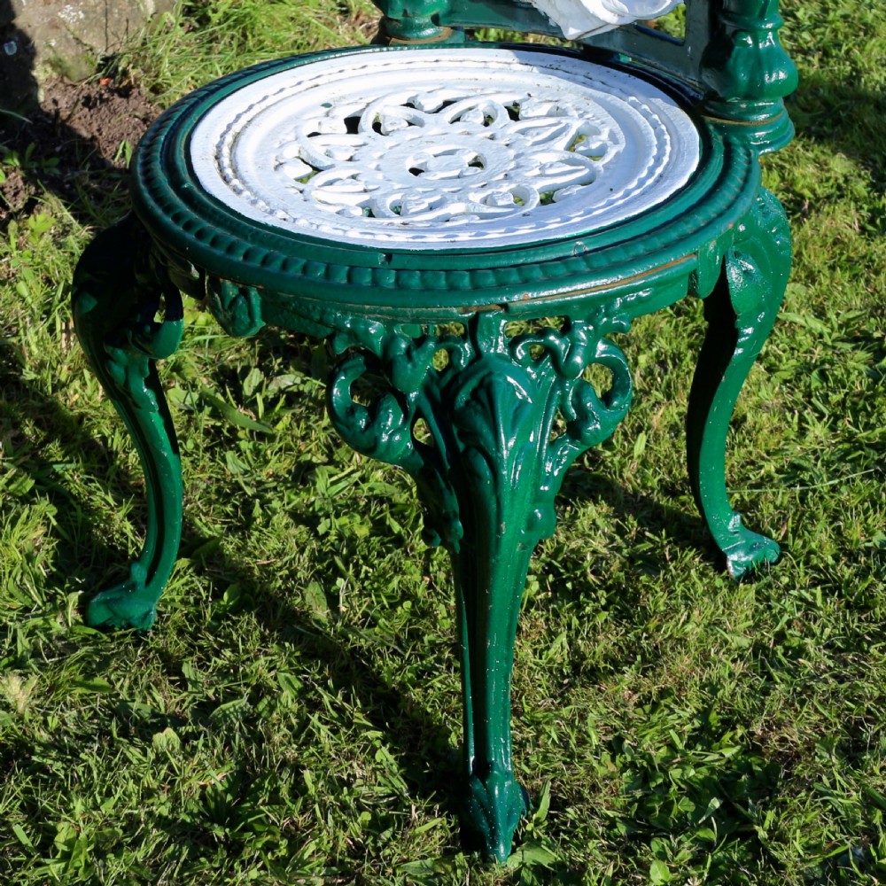 A set of four Victorian cast iron garden chairs featuring white openwork backrests with central medallion cameos framed by dark green structural frames and cabriole legs. View XVI