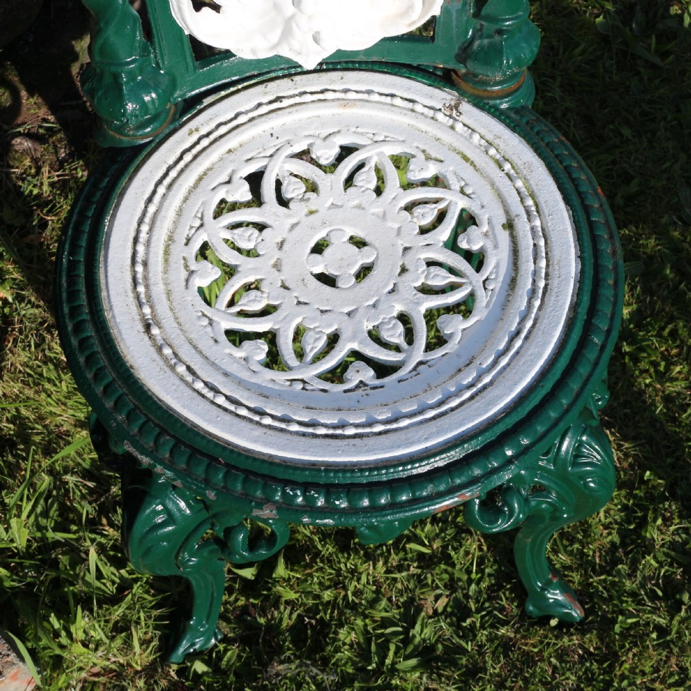 A set of four Victorian cast iron garden chairs featuring white openwork backrests with central medallion cameos framed by dark green structural frames and cabriole legs. View XVII