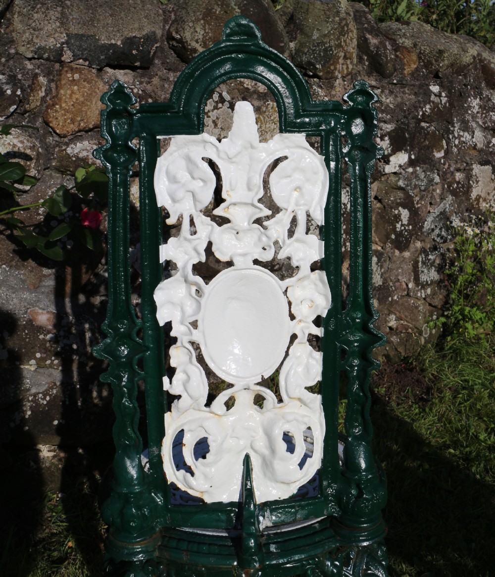 A set of four Victorian cast iron garden chairs featuring white openwork backrests with central medallion cameos framed by dark green structural frames and cabriole legs. View XXI