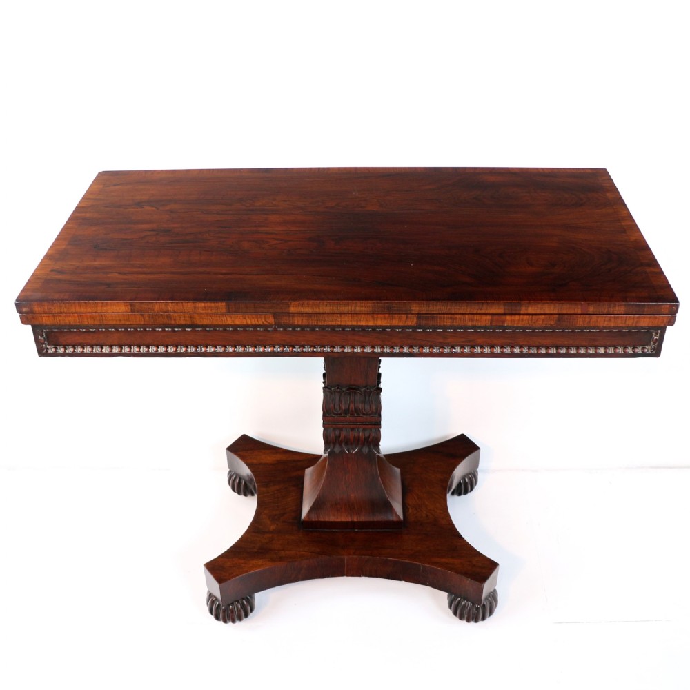 A Regency rosewood tea table featuring a rectangular fold-over top, bead moulding trim, a carved central pedestal, and a quadform base on carved feet.