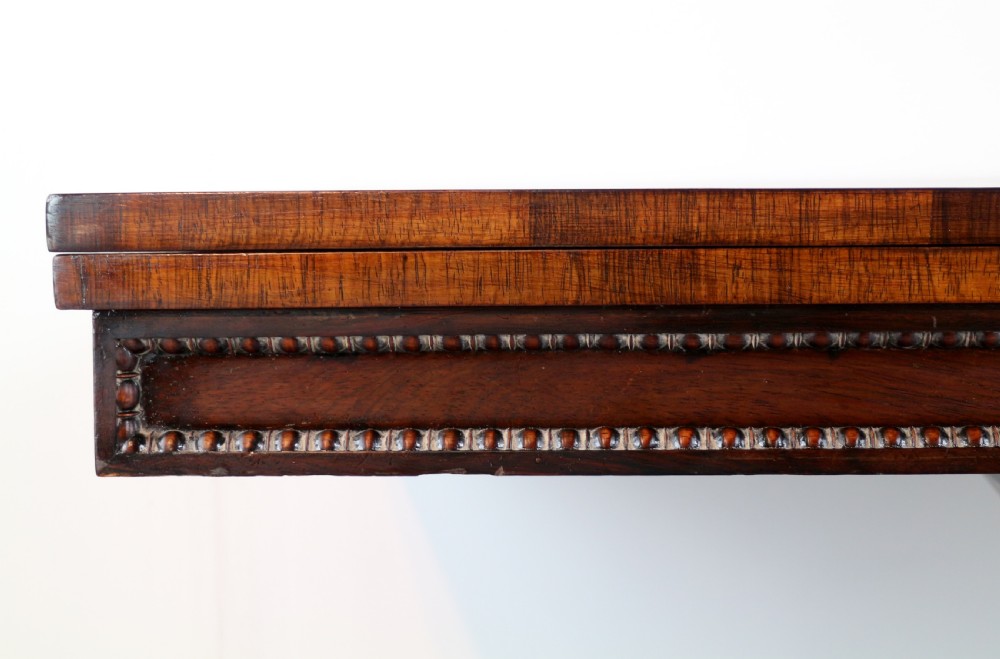 A Regency rosewood tea table featuring a rectangular fold-over top, bead moulding trim, a carved central pedestal, and a quadform base on carved feet. View VII