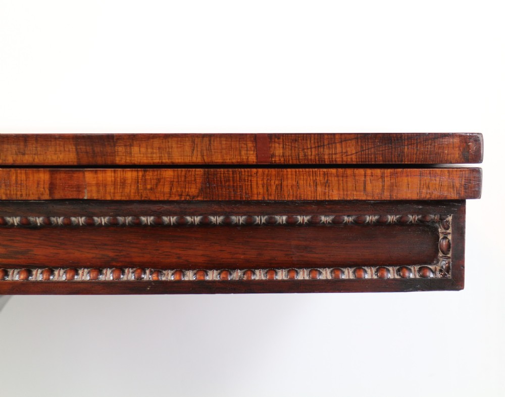 A Regency rosewood tea table featuring a rectangular fold-over top, bead moulding trim, a carved central pedestal, and a quadform base on carved feet. View IX