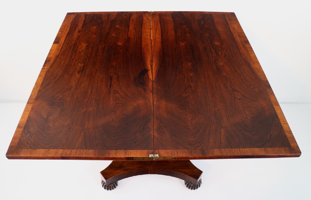 A Regency rosewood tea table featuring a rectangular fold-over top, bead moulding trim, a carved central pedestal, and a quadform base on carved feet. View XVI