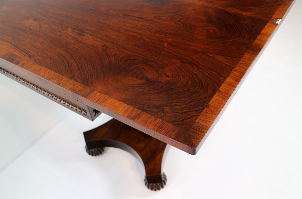 A Regency rosewood tea table featuring a rectangular fold-over top, bead moulding trim, a carved central pedestal, and a quadform base on carved feet. View XIX