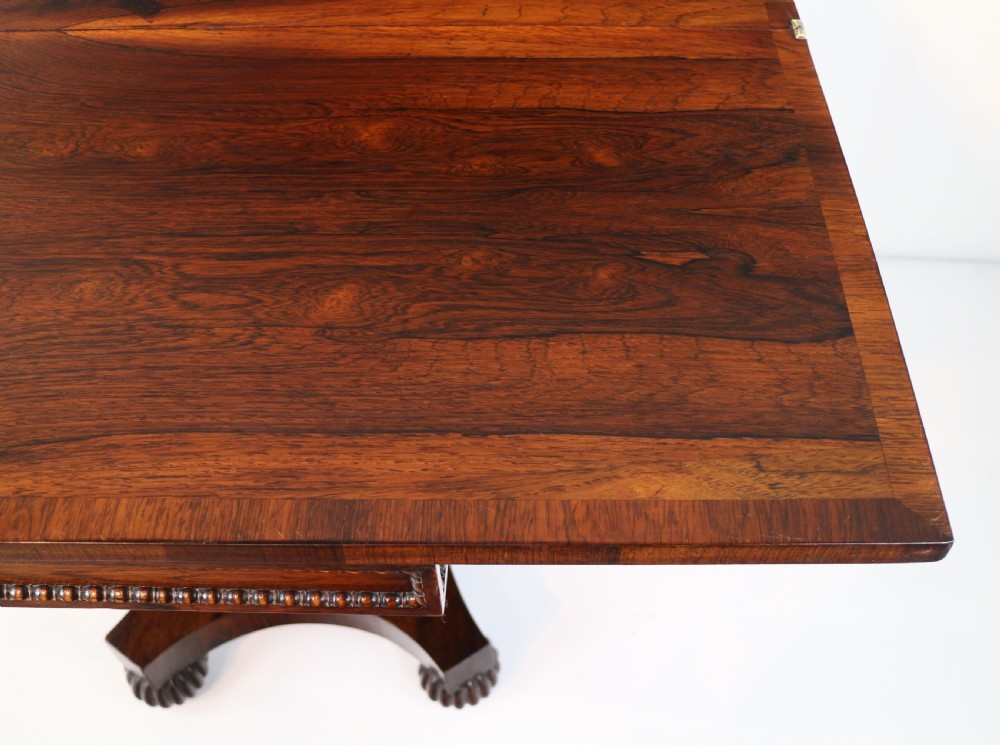 A Regency rosewood tea table featuring a rectangular fold-over top, bead moulding trim, a carved central pedestal, and a quadform base on carved feet. View XXI