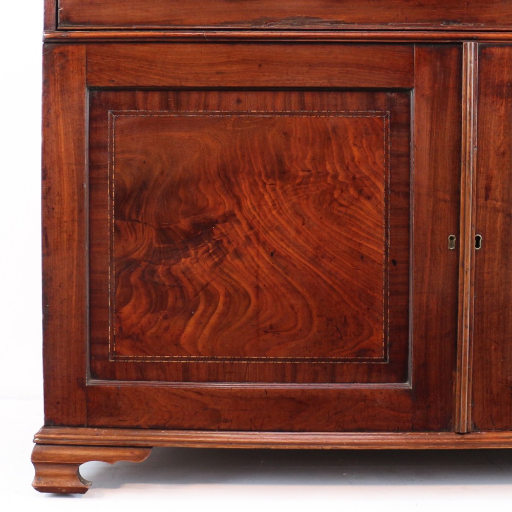 A George III mahogany secretaire low press cupboard featuring flame mahogany veneer panels, brass swan-neck handles, and bracket feet. View VIII
