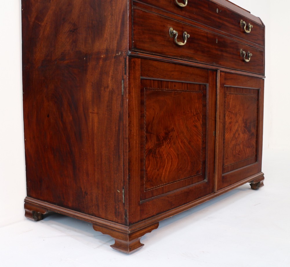 A George III mahogany secretaire low press cupboard featuring flame mahogany veneer panels, brass swan-neck handles, and bracket feet. View XXX
