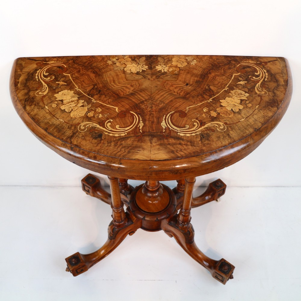 A Victorian burr walnut demilune card table featuring floral marquetry inlays, turned twin-column supports, and a carved central finial on quadruped legs. View II