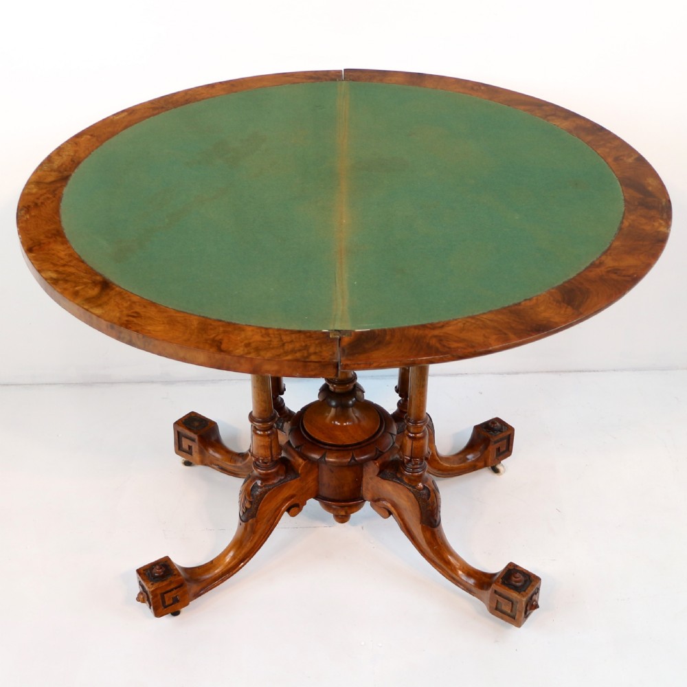 A Victorian burr walnut demilune card table featuring floral marquetry inlays, turned twin-column supports, and a carved central finial on quadruped legs. View VI