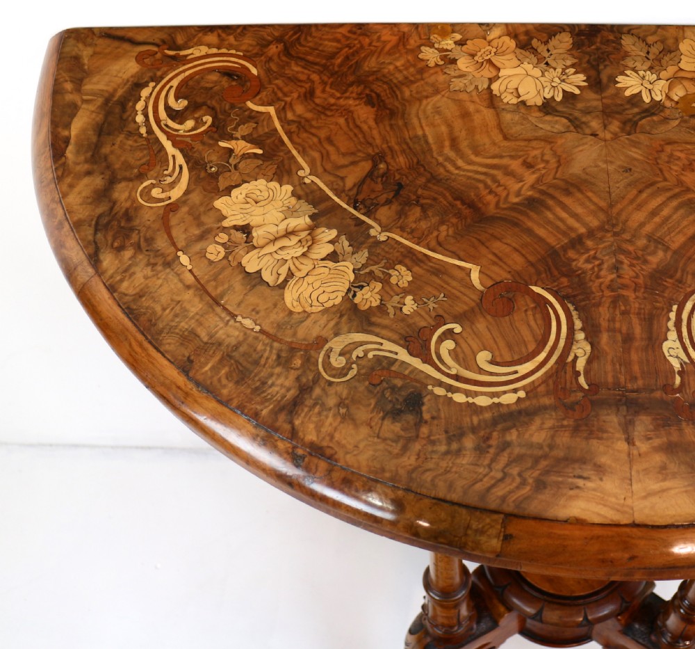 A Victorian burr walnut demilune card table featuring floral marquetry inlays, turned twin-column supports, and a carved central finial on quadruped legs. View XII