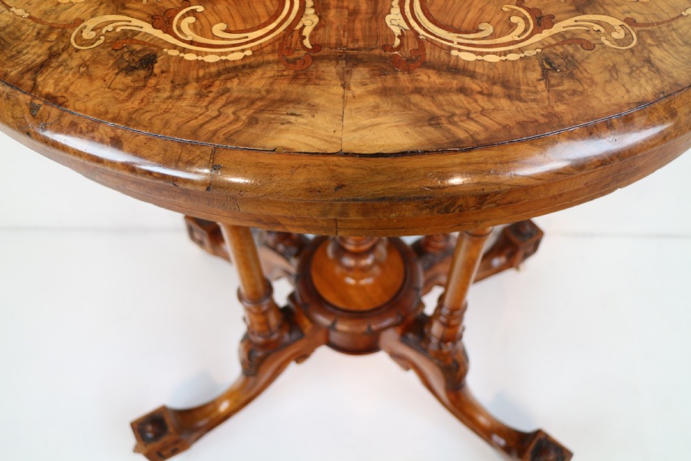 A Victorian burr walnut demilune card table featuring floral marquetry inlays, turned twin-column supports, and a carved central finial on quadruped legs. View XVI