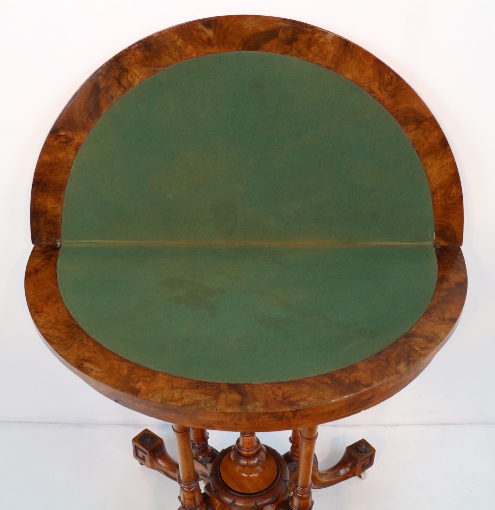 A Victorian burr walnut demilune card table featuring floral marquetry inlays, turned twin-column supports, and a carved central finial on quadruped legs. View XVIII