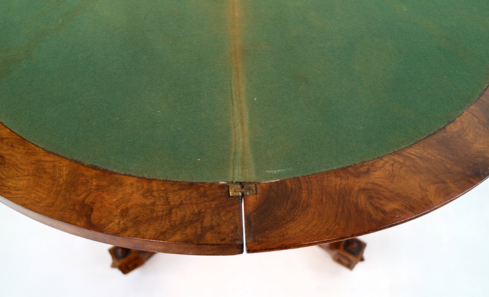 A Victorian burr walnut demilune card table featuring floral marquetry inlays, turned twin-column supports, and a carved central finial on quadruped legs. View XIX