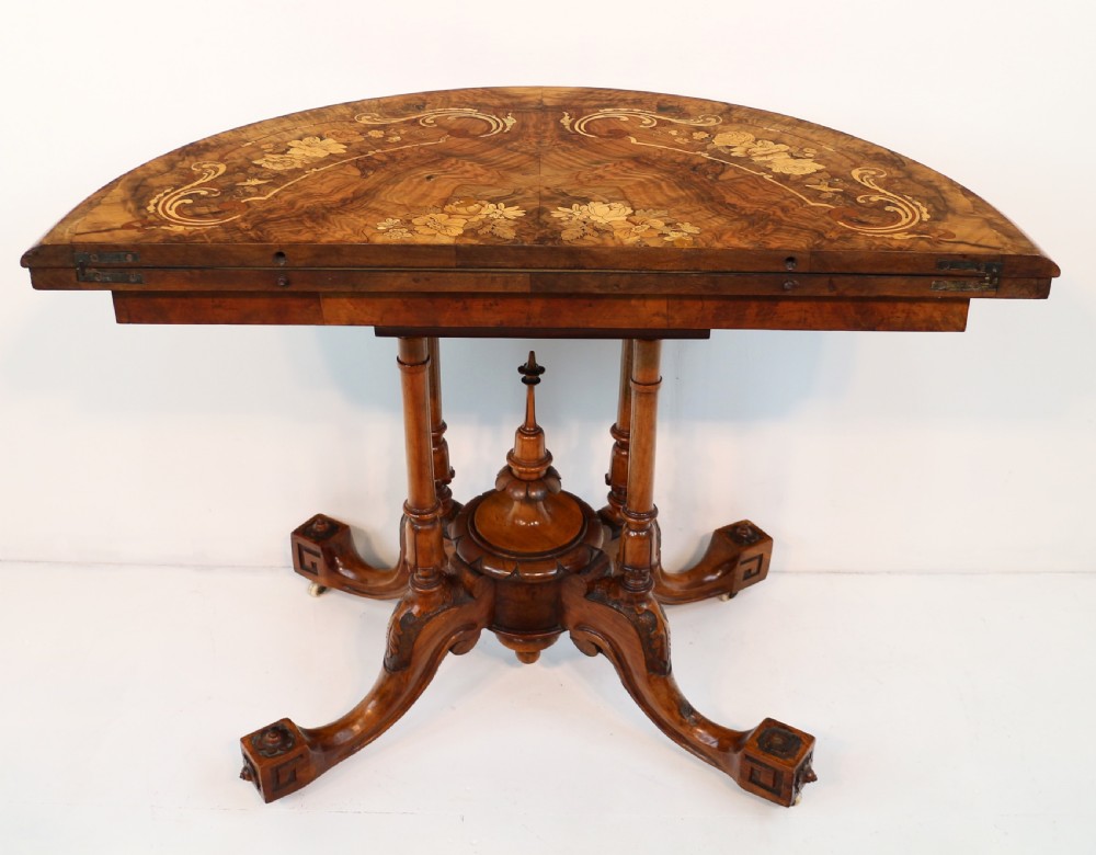 A Victorian burr walnut demilune card table featuring floral marquetry inlays, turned twin-column supports, and a carved central finial on quadruped legs. View XXI