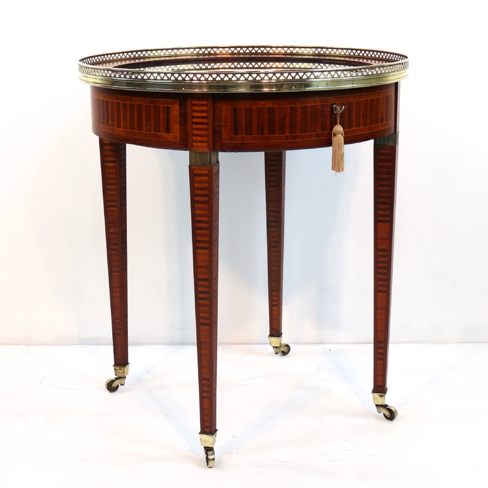 A circular Victorian rosewood bijouterie table featuring a glazed display lid, pierced brass rim gallery, inlaid tapered legs, and brass castors. View V
