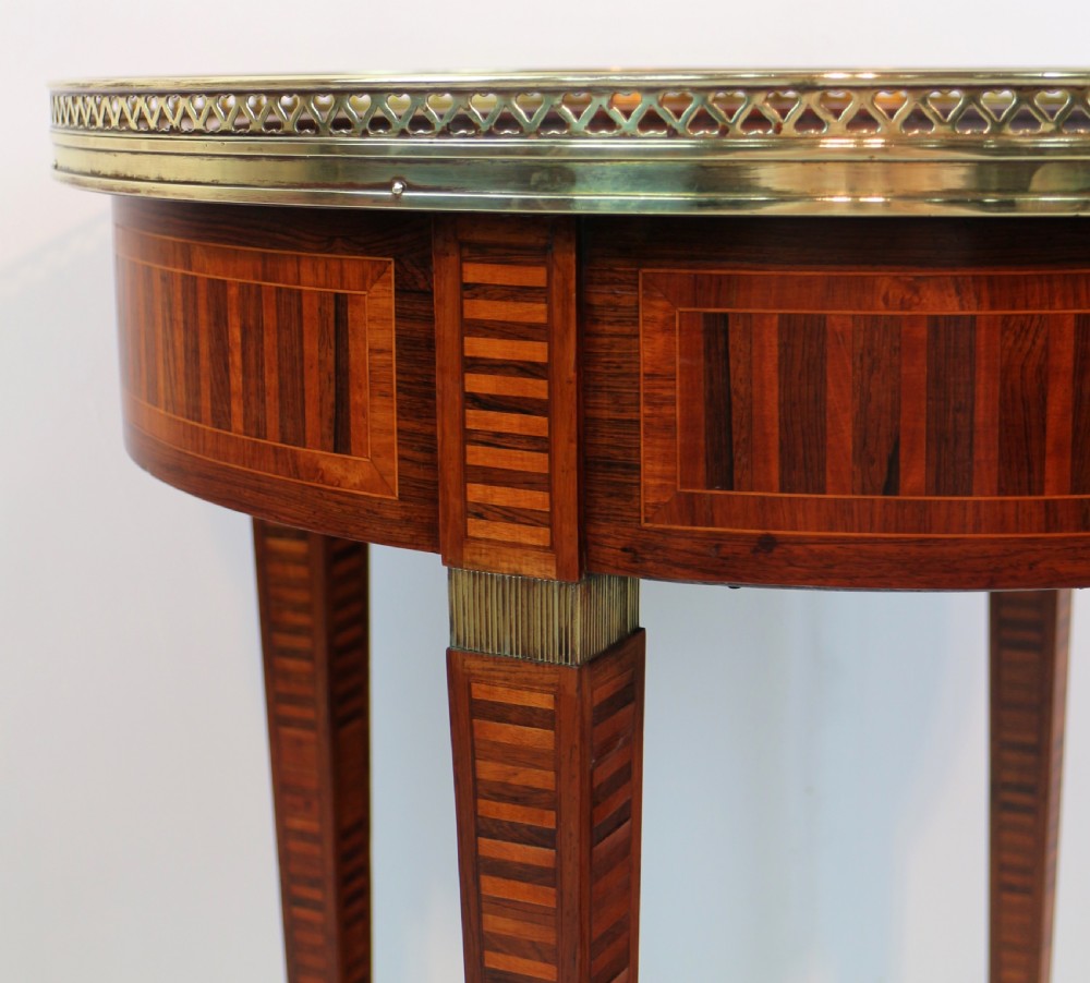 A circular Victorian rosewood bijouterie table featuring a glazed display lid, pierced brass rim gallery, inlaid tapered legs, and brass castors. View IX