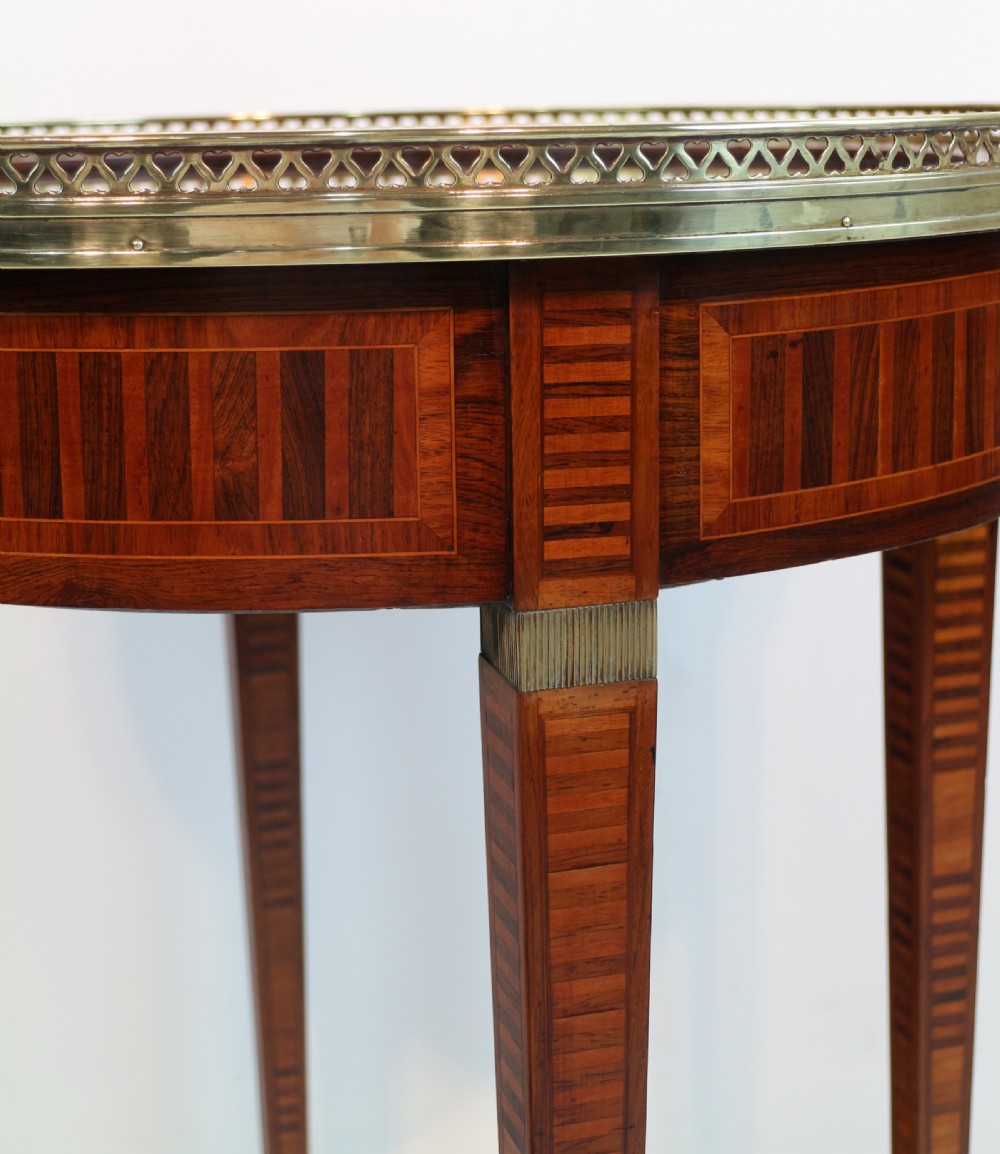 A circular Victorian rosewood bijouterie table featuring a glazed display lid, pierced brass rim gallery, inlaid tapered legs, and brass castors. View X