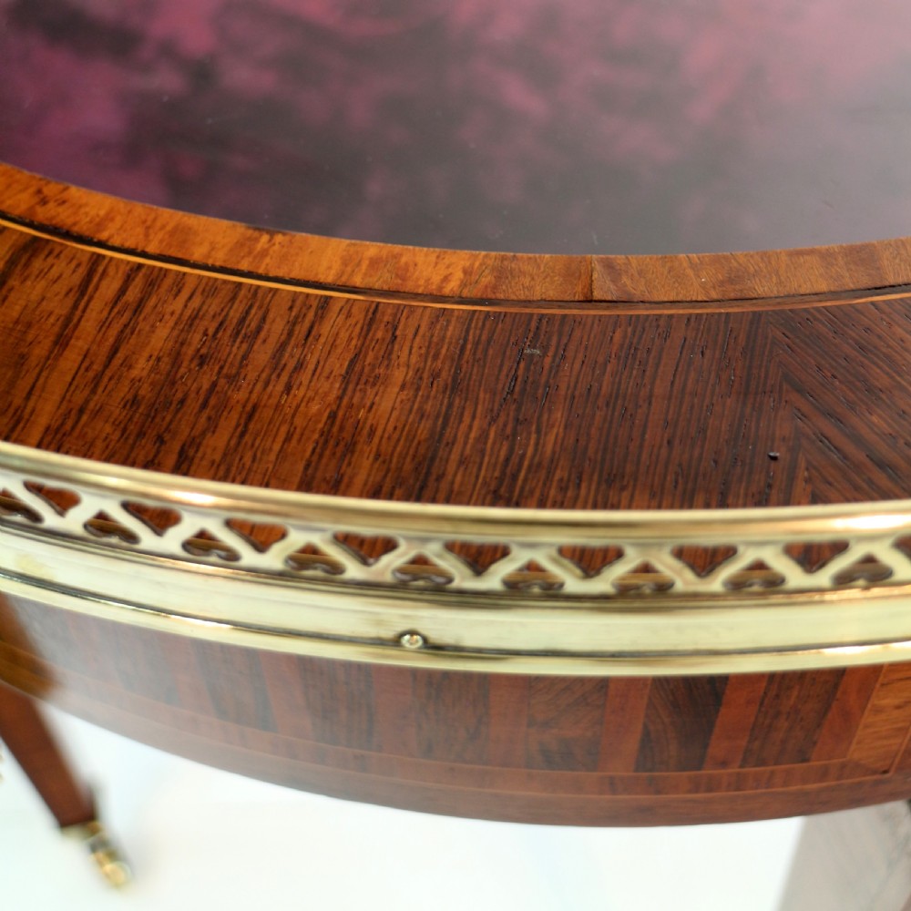 A circular Victorian rosewood bijouterie table featuring a glazed display lid, pierced brass rim gallery, inlaid tapered legs, and brass castors. View XVI