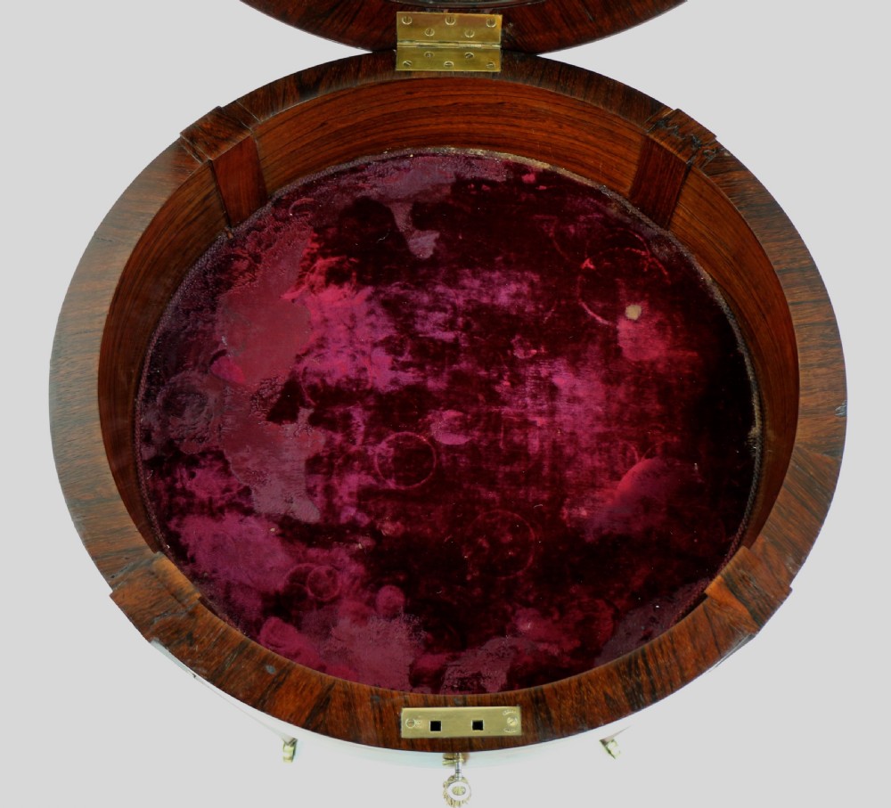 A circular Victorian rosewood bijouterie table featuring a glazed display lid, pierced brass rim gallery, inlaid tapered legs, and brass castors. View XVIII