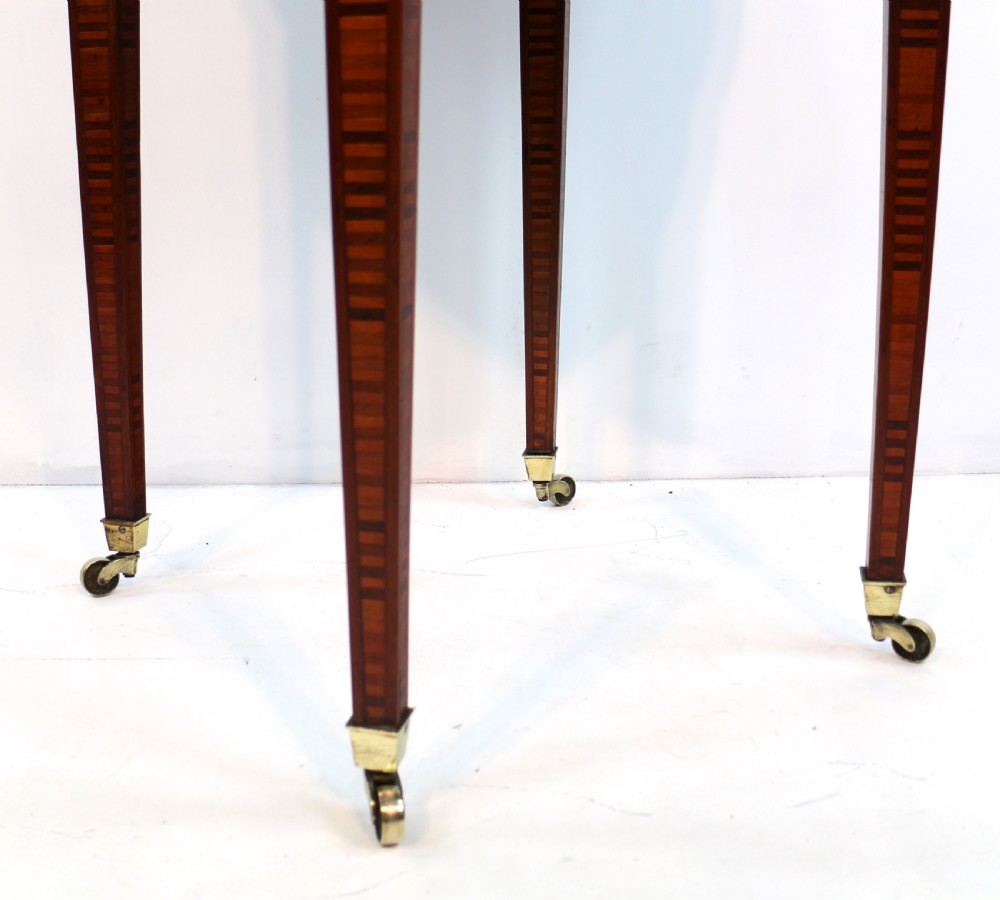 A circular Victorian rosewood bijouterie table featuring a glazed display lid, pierced brass rim gallery, inlaid tapered legs, and brass castors. View XX