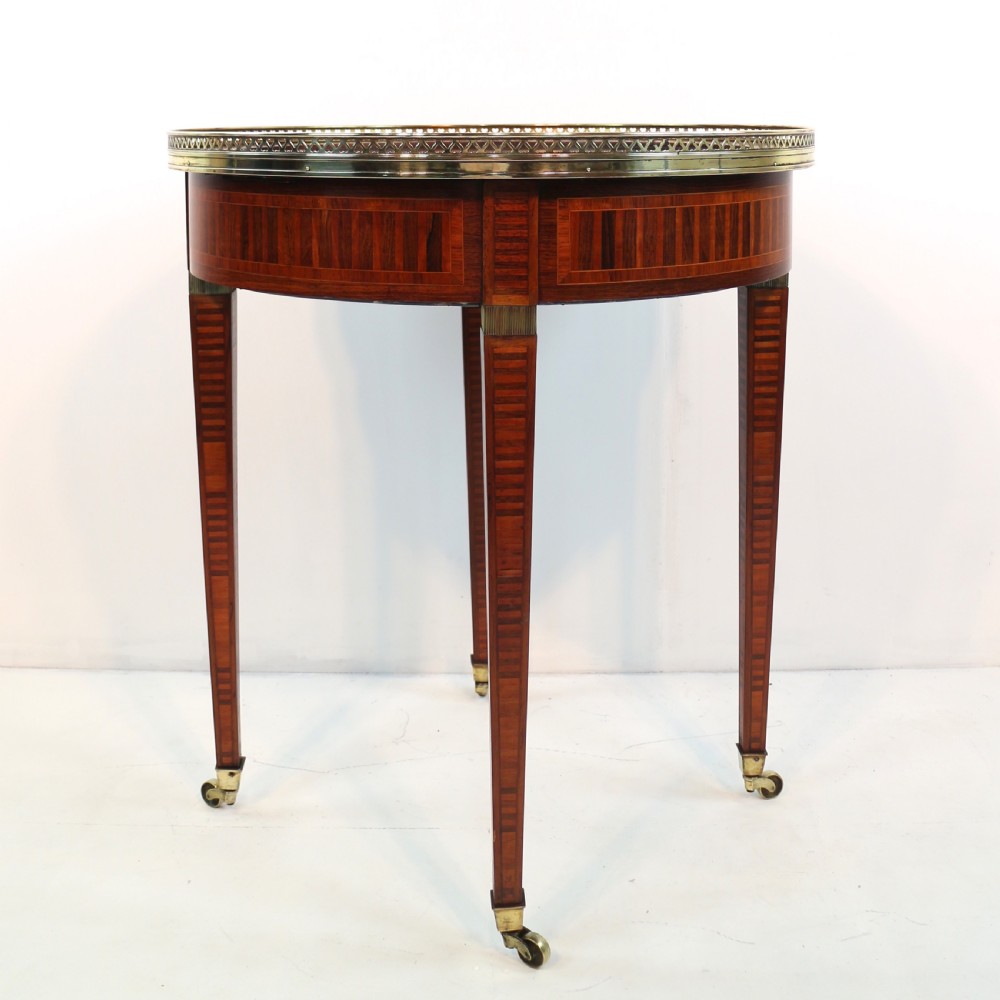 A circular Victorian rosewood bijouterie table featuring a glazed display lid, pierced brass rim gallery, inlaid tapered legs, and brass castors. View XXIII