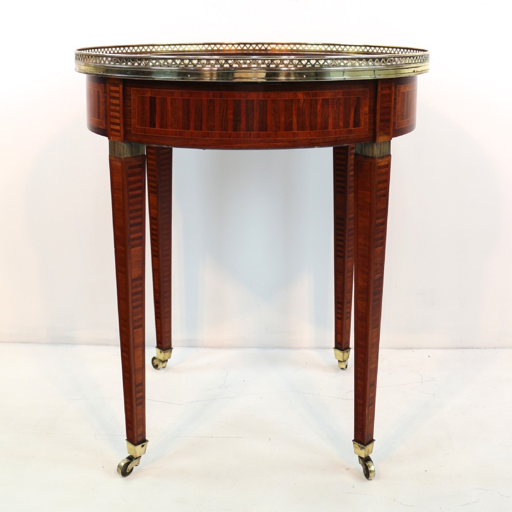 A circular Victorian rosewood bijouterie table featuring a glazed display lid, pierced brass rim gallery, inlaid tapered legs, and brass castors. View XXIV