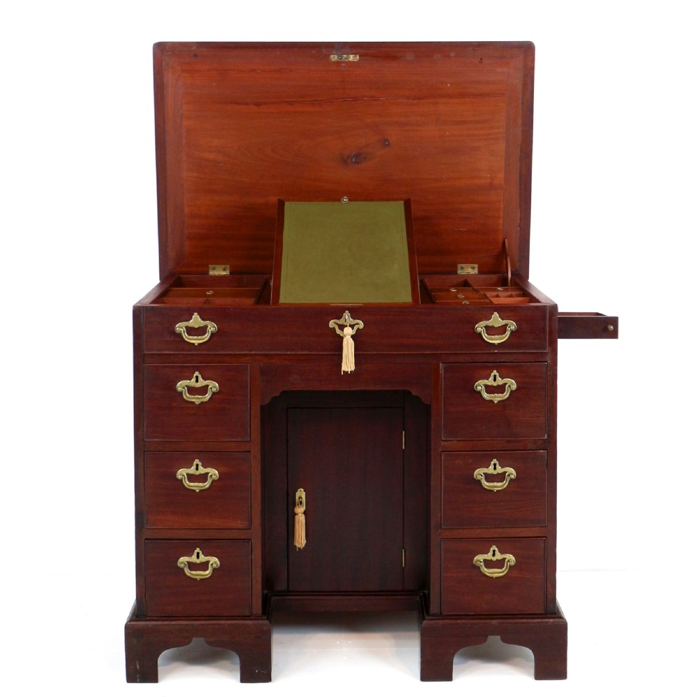 An antique George II red walnut kneehole desk featuring a hinged top that opens to reveal internal compartments and an adjustable green leather mirror, resting on bracket feet with brass handles.