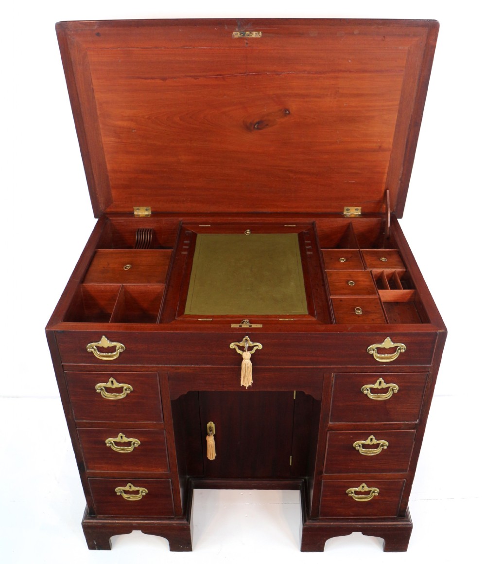 An antique George II red walnut kneehole desk featuring a hinged top that opens to reveal internal compartments and an adjustable green leather mirror, resting on bracket feet with brass handles. View III