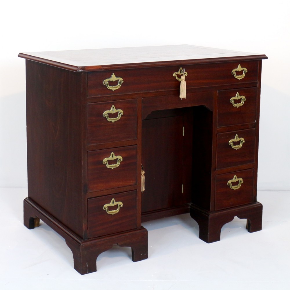 An antique George II red walnut kneehole desk featuring a hinged top that opens to reveal internal compartments and an adjustable green leather mirror, resting on bracket feet with brass handles. View IV