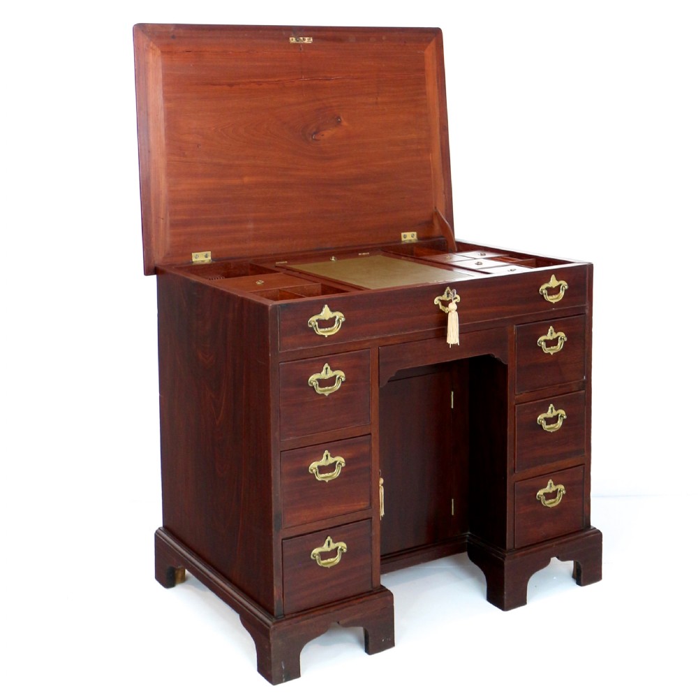 An antique George II red walnut kneehole desk featuring a hinged top that opens to reveal internal compartments and an adjustable green leather mirror, resting on bracket feet with brass handles. View V