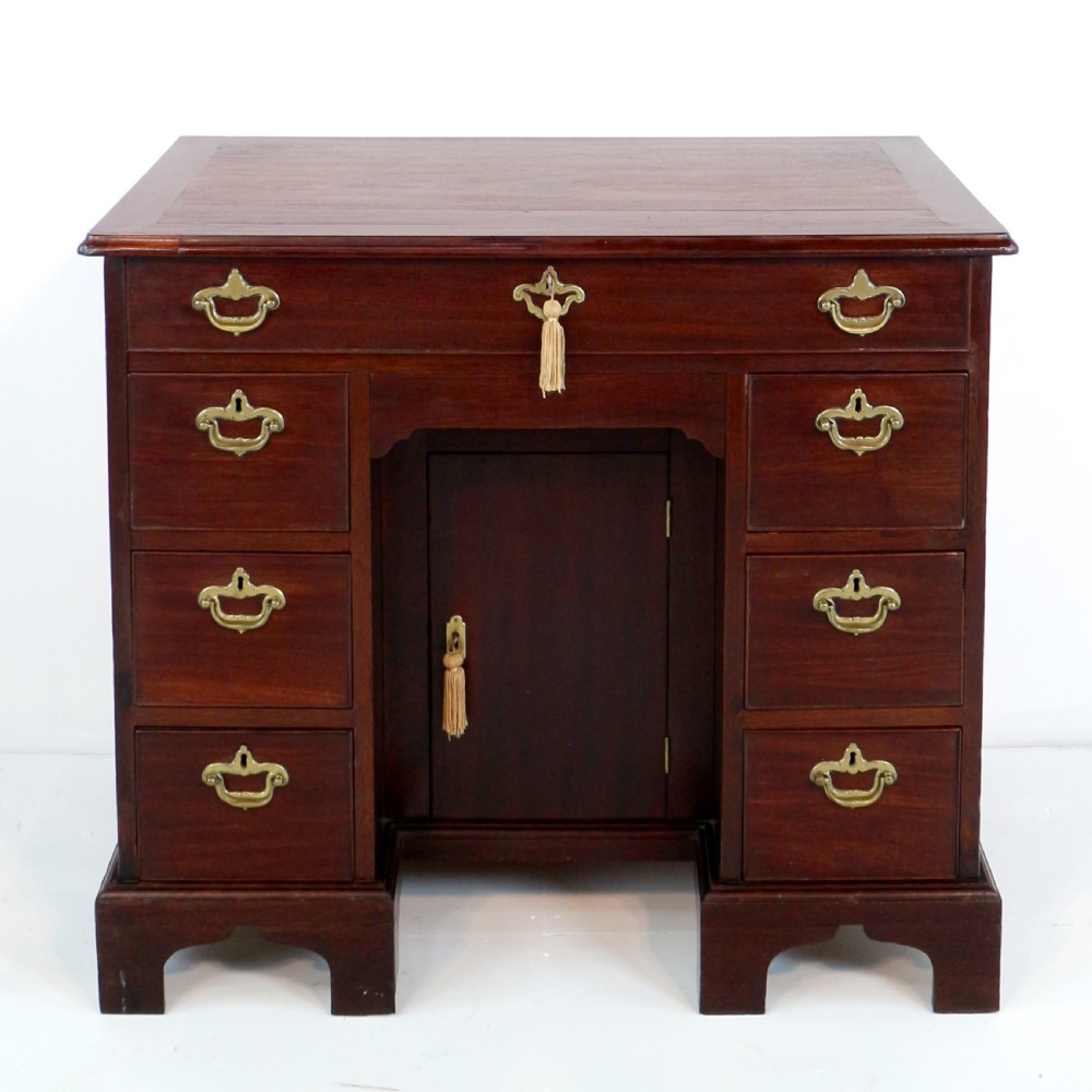 An antique George II red walnut kneehole desk featuring a hinged top that opens to reveal internal compartments and an adjustable green leather mirror, resting on bracket feet with brass handles. View VI