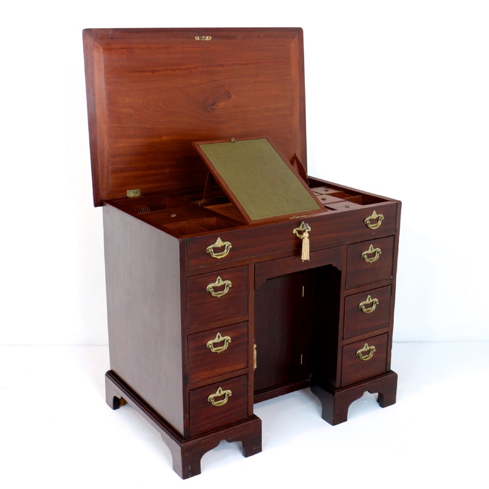 An antique George II red walnut kneehole desk featuring a hinged top that opens to reveal internal compartments and an adjustable green leather mirror, resting on bracket feet with brass handles. View VII