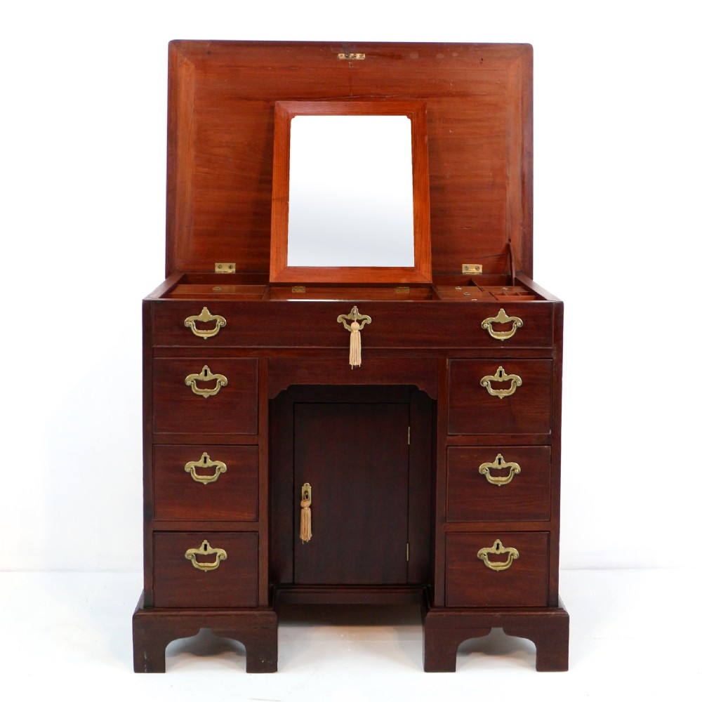 An antique George II red walnut kneehole desk featuring a hinged top that opens to reveal internal compartments and an adjustable green leather mirror, resting on bracket feet with brass handles. View IX
