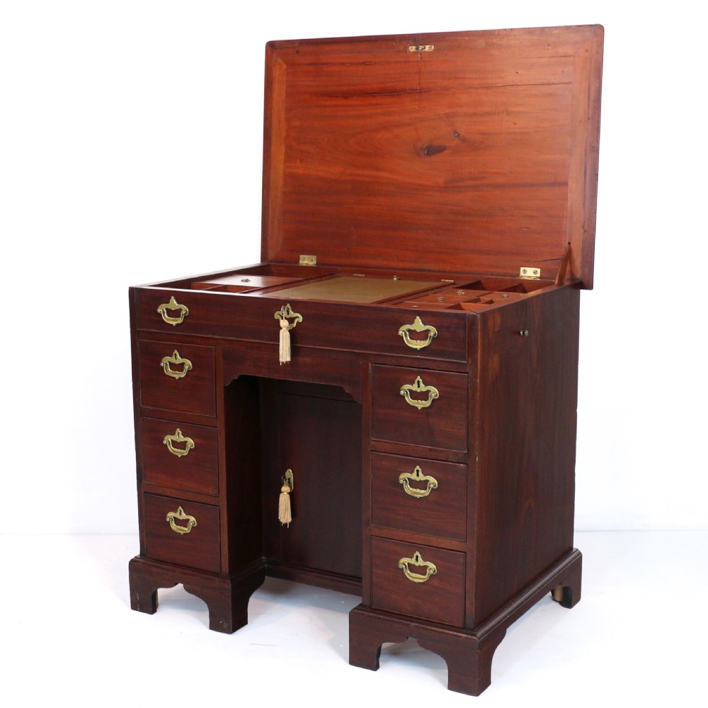 An antique George II red walnut kneehole desk featuring a hinged top that opens to reveal internal compartments and an adjustable green leather mirror, resting on bracket feet with brass handles. View X