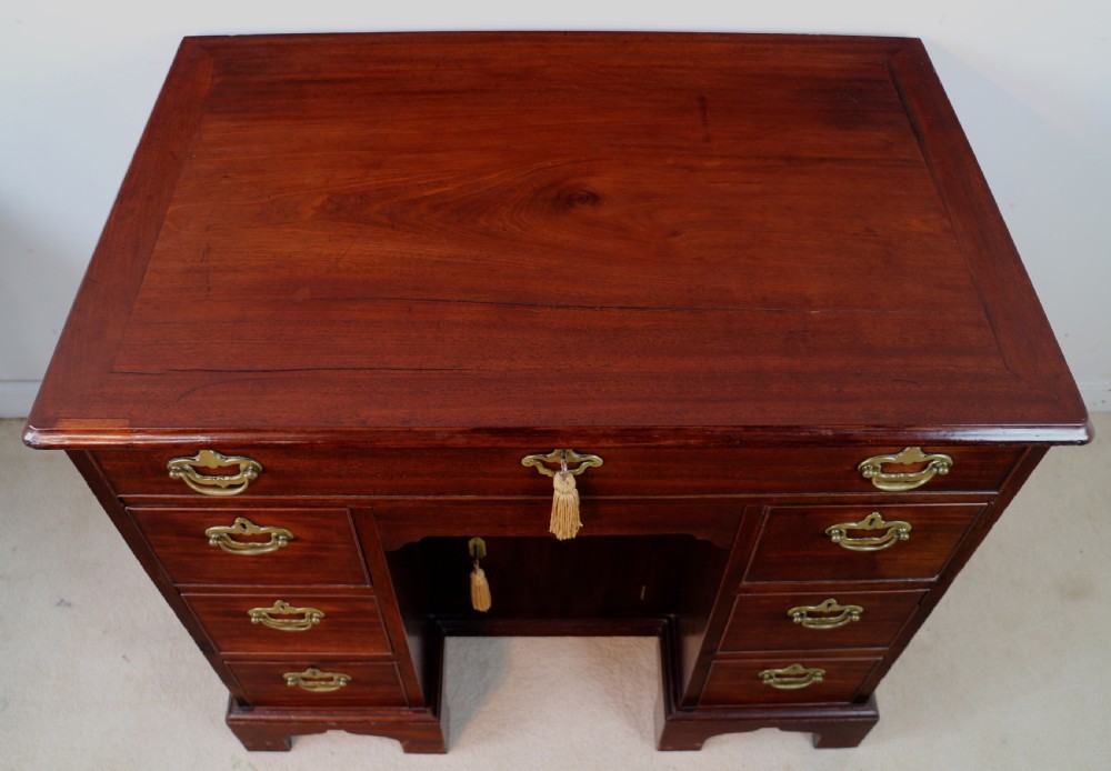 An antique George II red walnut kneehole desk featuring a hinged top that opens to reveal internal compartments and an adjustable green leather mirror, resting on bracket feet with brass handles. View XIII