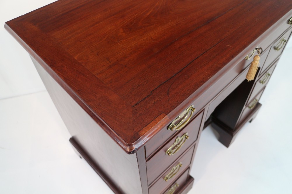 An antique George II red walnut kneehole desk featuring a hinged top that opens to reveal internal compartments and an adjustable green leather mirror, resting on bracket feet with brass handles. View XIV