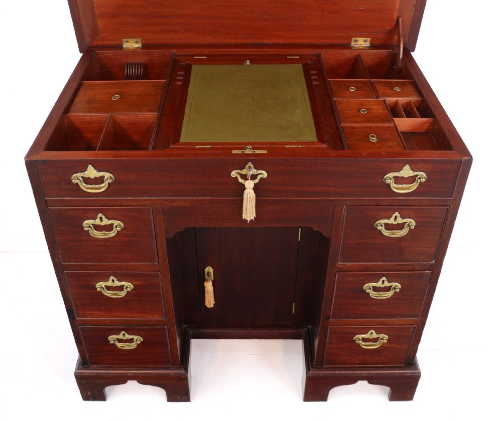An antique George II red walnut kneehole desk featuring a hinged top that opens to reveal internal compartments and an adjustable green leather mirror, resting on bracket feet with brass handles. View XV