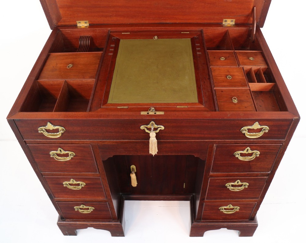 An antique George II red walnut kneehole desk featuring a hinged top that opens to reveal internal compartments and an adjustable green leather mirror, resting on bracket feet with brass handles. View XVI