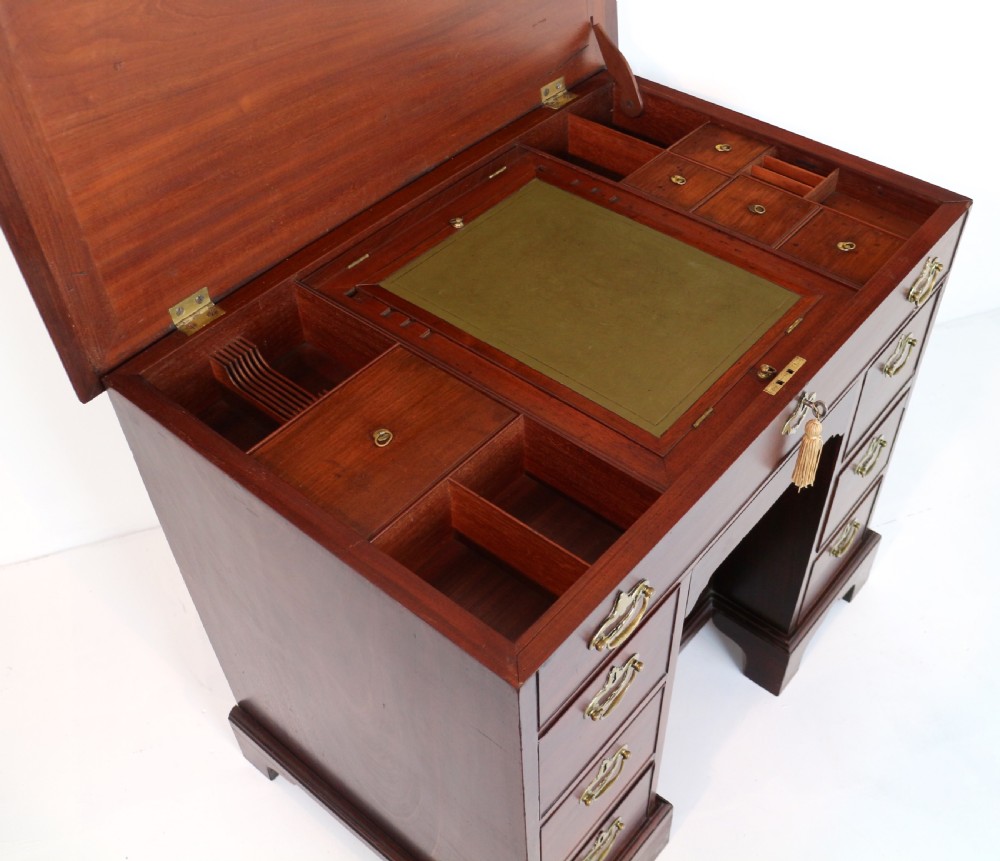 An antique George II red walnut kneehole desk featuring a hinged top that opens to reveal internal compartments and an adjustable green leather mirror, resting on bracket feet with brass handles. View XVII