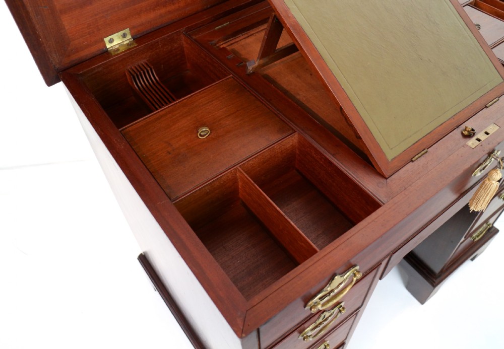 An antique George II red walnut kneehole desk featuring a hinged top that opens to reveal internal compartments and an adjustable green leather mirror, resting on bracket feet with brass handles. View XVIII