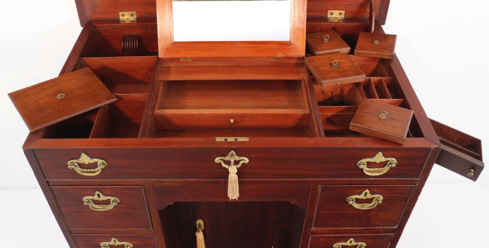 An antique George II red walnut kneehole desk featuring a hinged top that opens to reveal internal compartments and an adjustable green leather mirror, resting on bracket feet with brass handles. View XIX