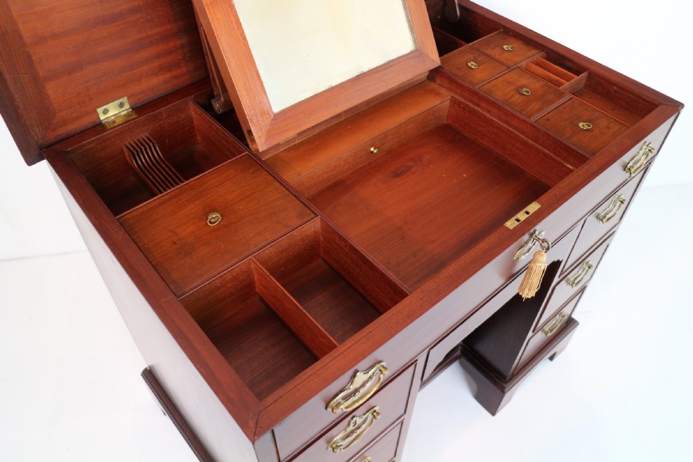 An antique George II red walnut kneehole desk featuring a hinged top that opens to reveal internal compartments and an adjustable green leather mirror, resting on bracket feet with brass handles. View XXI
