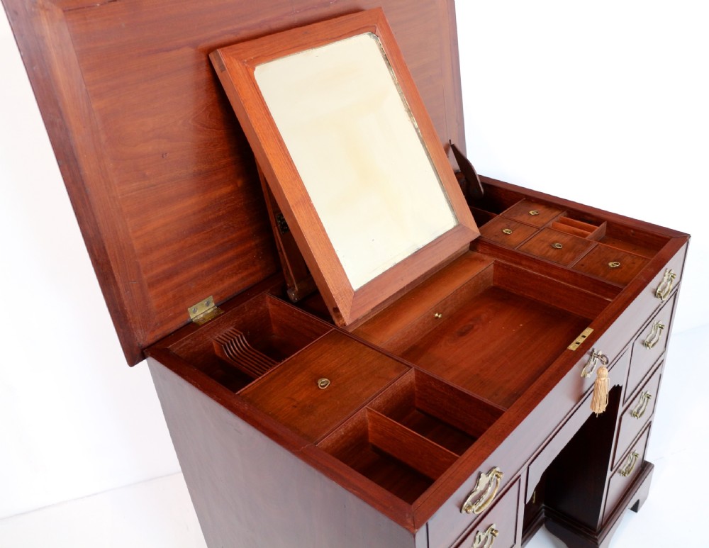 An antique George II red walnut kneehole desk featuring a hinged top that opens to reveal internal compartments and an adjustable green leather mirror, resting on bracket feet with brass handles. View XXIII