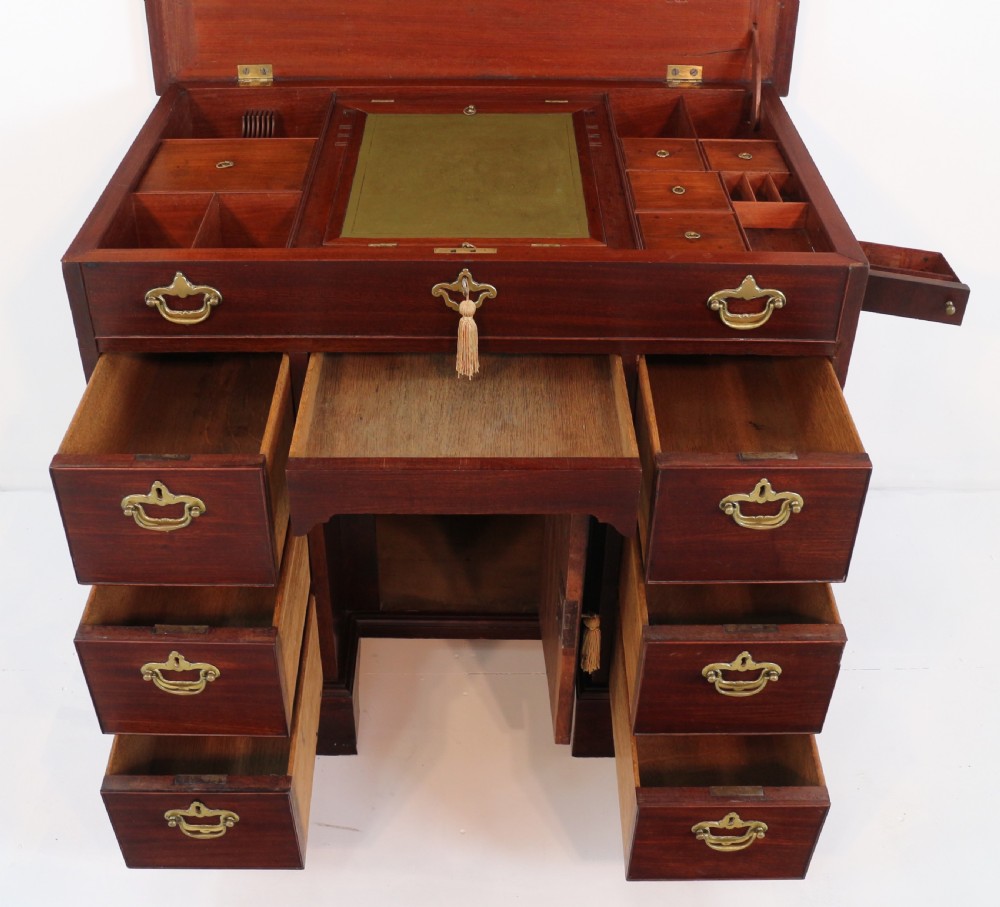 An antique George II red walnut kneehole desk featuring a hinged top that opens to reveal internal compartments and an adjustable green leather mirror, resting on bracket feet with brass handles. View XXIV